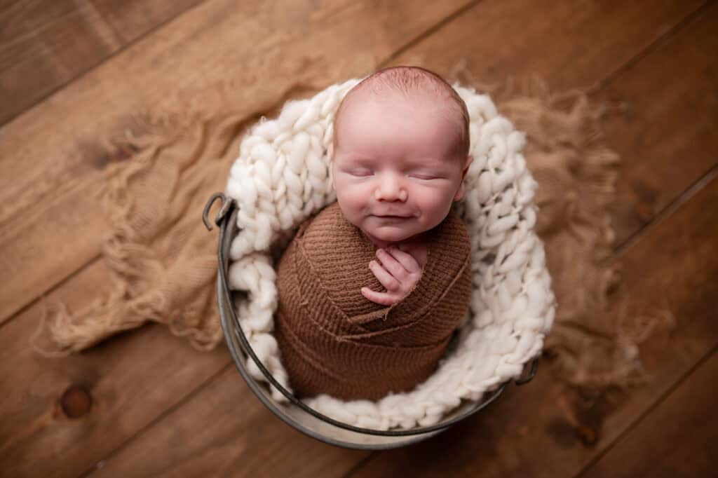 wrapped baby smiles in bucket photographed by wichita newborn photographer sj nuzum photography