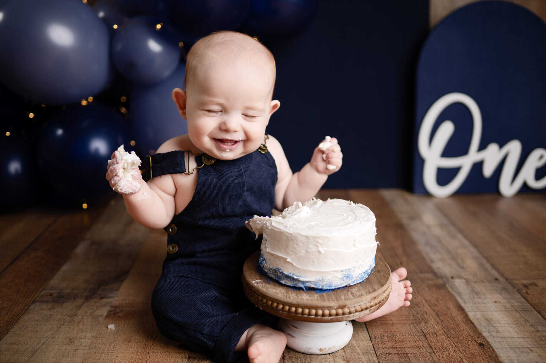 family photographer wichita ks smash cake photoshoot boy in blue smiles with cake